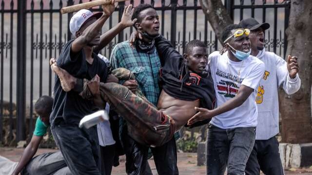 Protesters gesture as they carry an injured man outside the Kenya Parliament during a nationwide strike to protest against tax hikes and the Finance Bill 2024 in downtown Nairobi, on June 25, 2024. Kenyan police shot dead one protester near the country's parliament Tuesday, a rights watchdog said as demonstrators angry over proposed tax hikes breached barricades and entered the government complex, where a fire erupted. The mainly Gen-Z-led rallies, which began last week, have taken President William Ruto's government by surprise, with the Kenyan leader saying over the weekend that he was ready to speak to the protesters. (Photo by LUIS TATO / AFP)